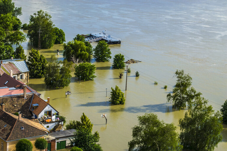 a flooded area with houses and a boat in the water - Hurricane Damage Claims Adjuster